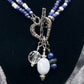 Necklace with blue and white beads and a silver heart-shaped toggle clasp on a black stand.