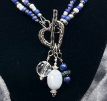 Necklace with blue and white beads and a silver heart-shaped toggle clasp on a black stand.