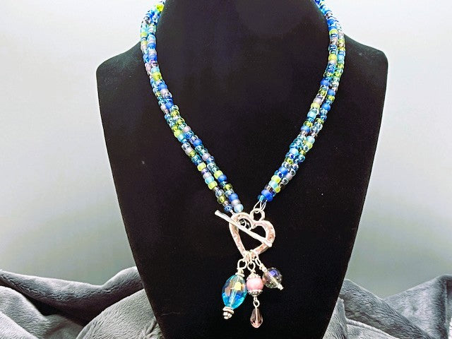 Beaded necklace with a heart toggle closure featuring charms on a black mannequin against a neutral background